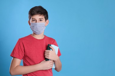 Boy wearing protective mask with books on light blue background, space for text. Child safety