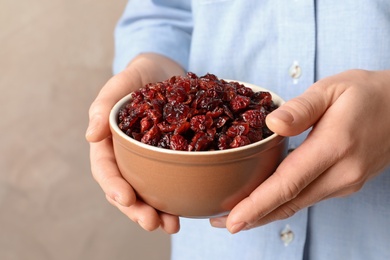 Woman holding bowl with tasty cranberries on color background, closeup. Dried fruits as healthy snack