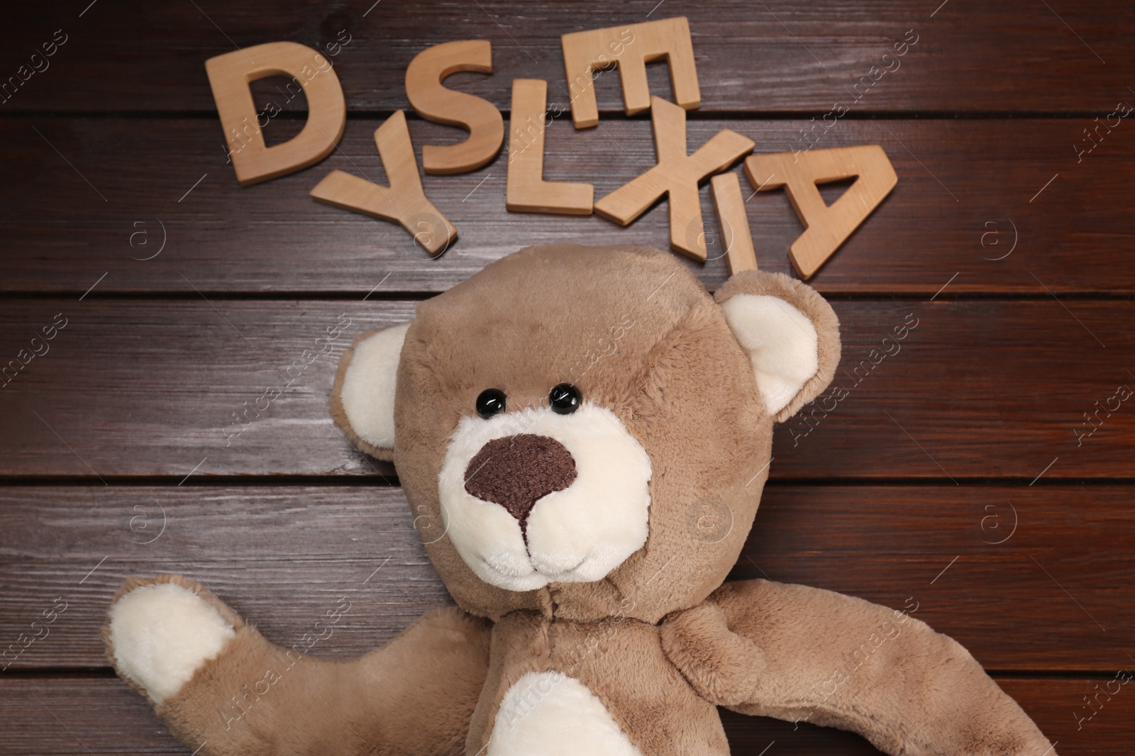 Photo of Word Dyslexia made of letters and teddy bear on wooden table, flat lay