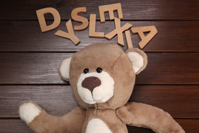 Photo of Word Dyslexia made of letters and teddy bear on wooden table, flat lay