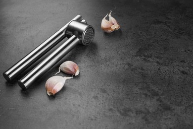 Photo of Garlic press and cloves on grey table. Space for text