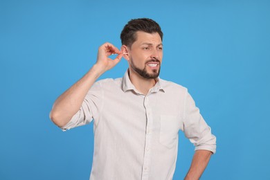 Emotional man cleaning ears on light blue background