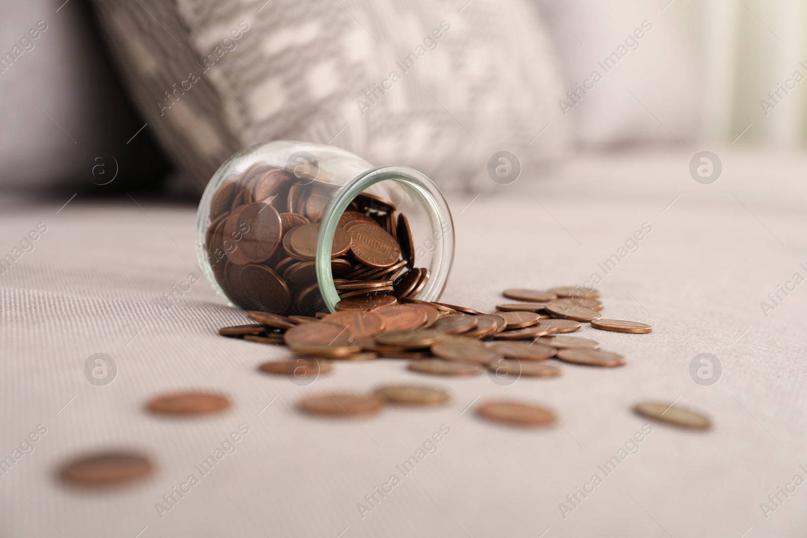 Photo of Overturned glass jar with coins on grey sofa
