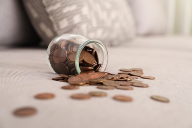 Overturned glass jar with coins on grey sofa