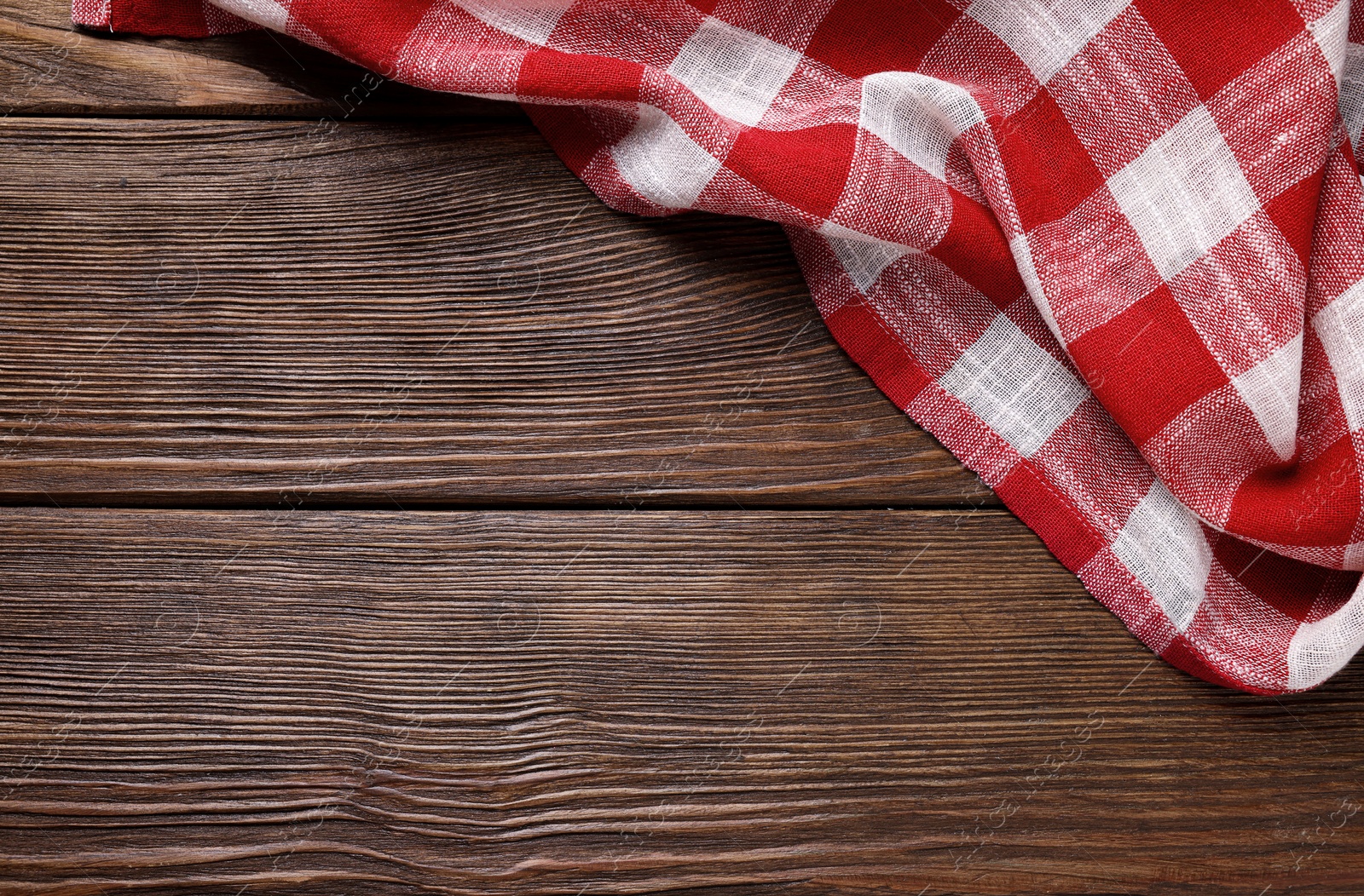 Photo of Red checkered tablecloth on wooden table, top view. Space for text