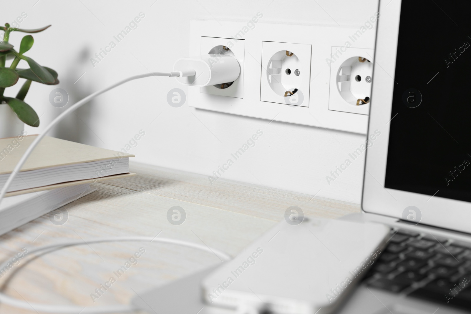 Photo of Laptop and smartphone charging on wooden table, closeup