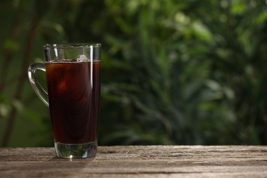 Photo of Glass of iced coffee on wooden table outdoors. Space for text