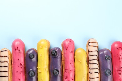 Photo of Delicious eclairs covered with glaze on light blue background, top view. Space for text