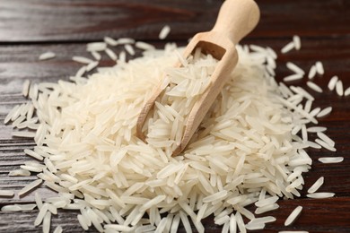 Photo of Raw basmati rice and scoop on wooden table, closeup