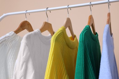 Rack with different warm sweaters on beige background