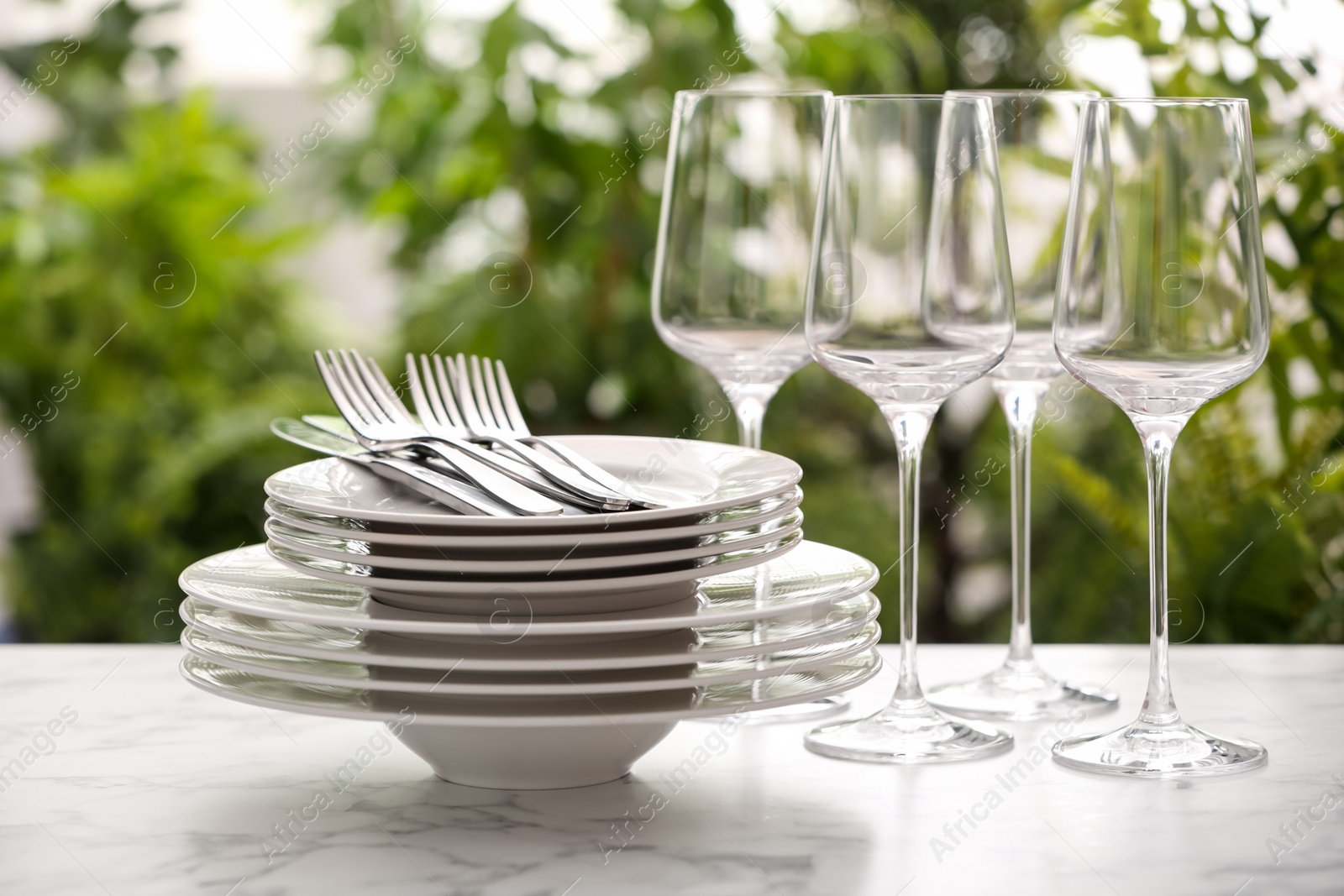 Photo of Set of clean dishware, cutlery and wineglasses on white table against blurred background