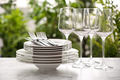 Photo of Set of clean dishware, cutlery and wineglasses on white table against blurred background