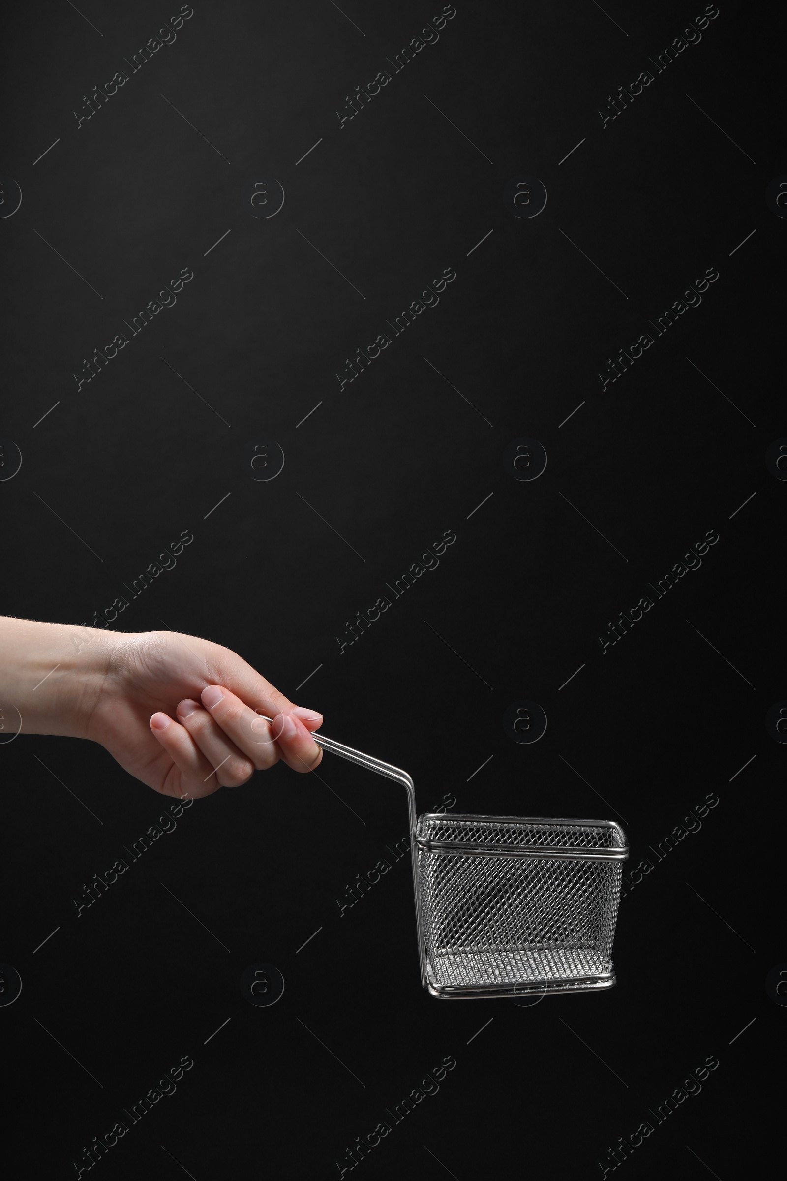 Photo of Woman holding metal basket for French fries on black background, closeup