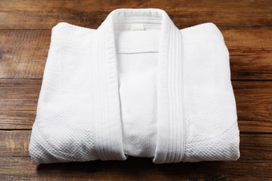 White kimono on wooden background, closeup. Martial arts uniform