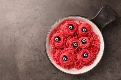 Red pasta with decorative eyes and olives in bowl on grey textured table, top view with space for text. Halloween food