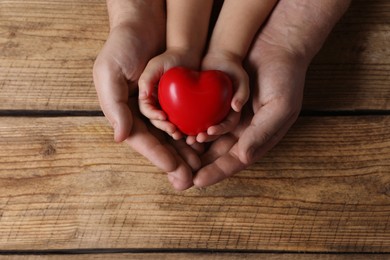 Father and his child holding red decorative heart at wooden table, top view. Space for text