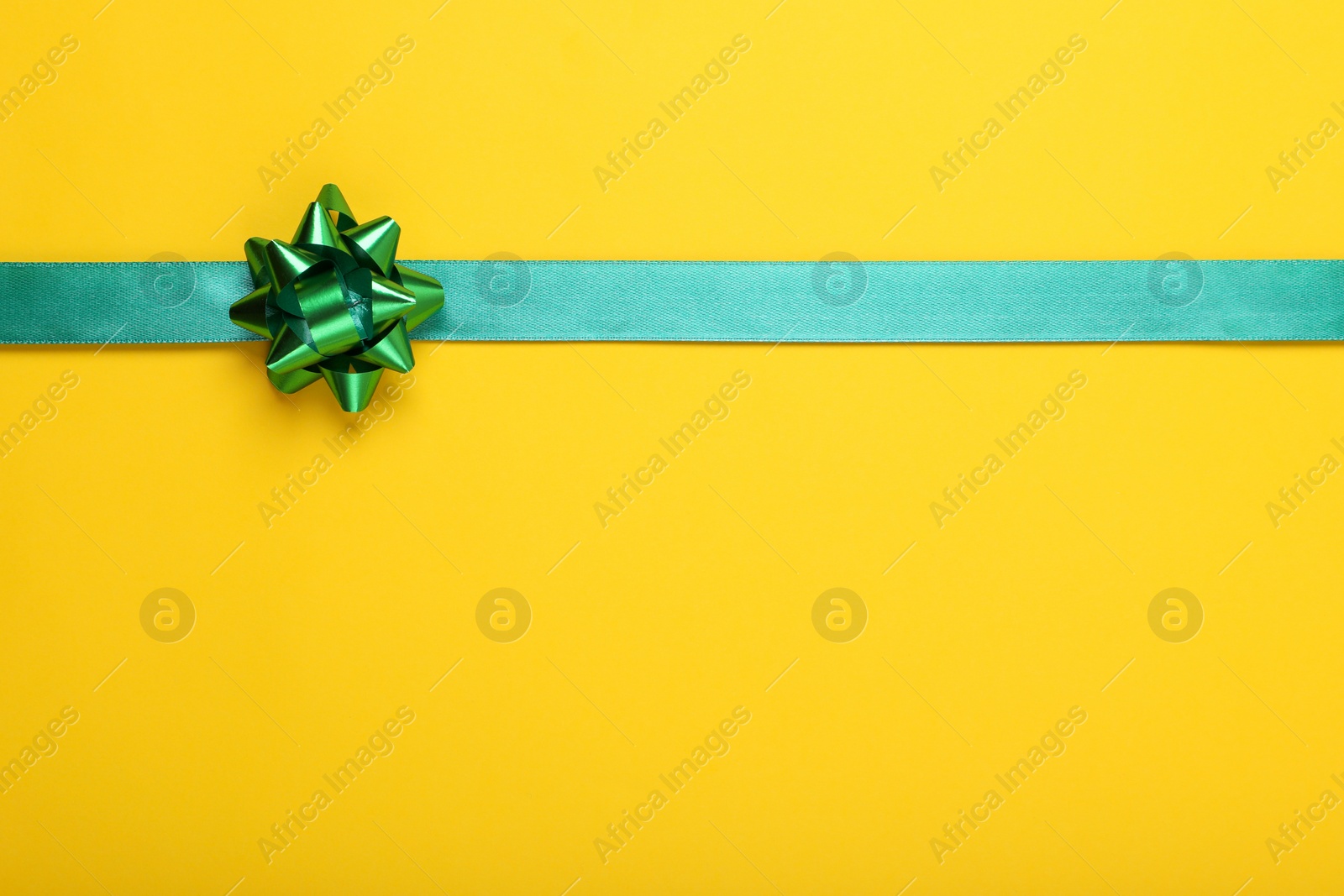 Photo of Green ribbon with bow on yellow background, top view. Space for text