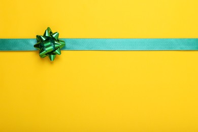 Photo of Green ribbon with bow on yellow background, top view. Space for text