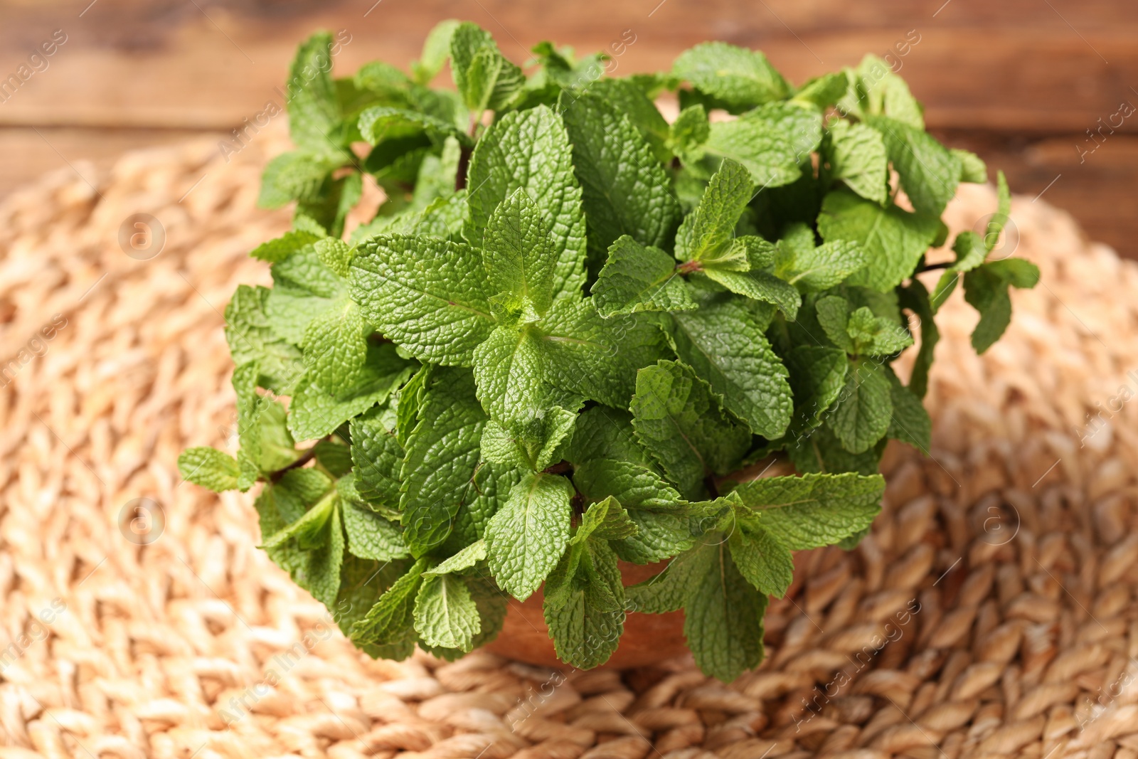 Photo of Bowl with fresh green mint leaves on wicker mat, closeup