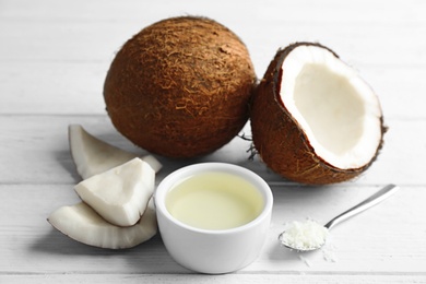 Bowl of natural organic oil and coconuts on white wooden background, closeup