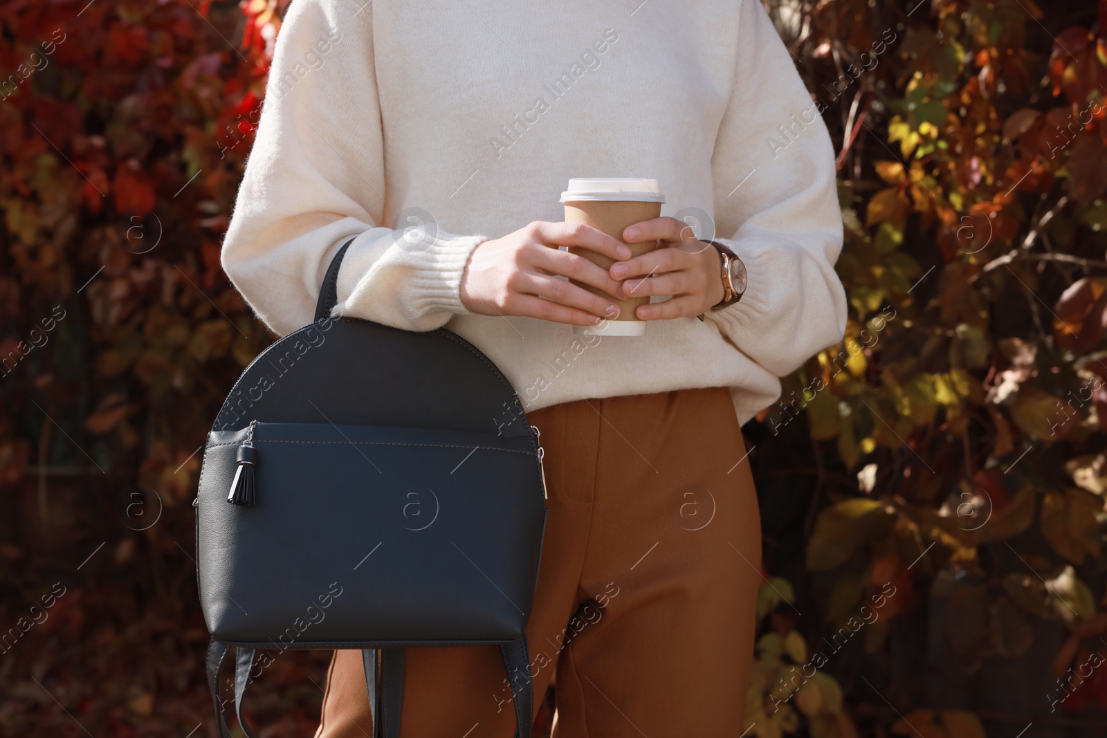 Photo of Young woman with stylish grey backpack and hot drink in autumn park, closeup