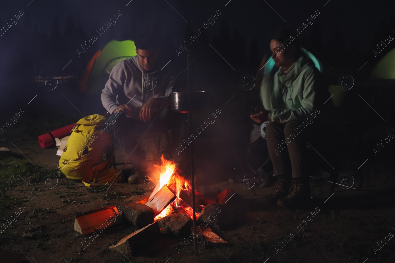 Photo of Couple near bonfire outdoors in evening. Camping season