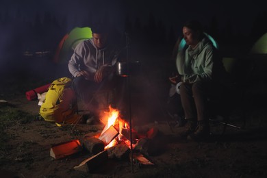 Photo of Couple near bonfire outdoors in evening. Camping season