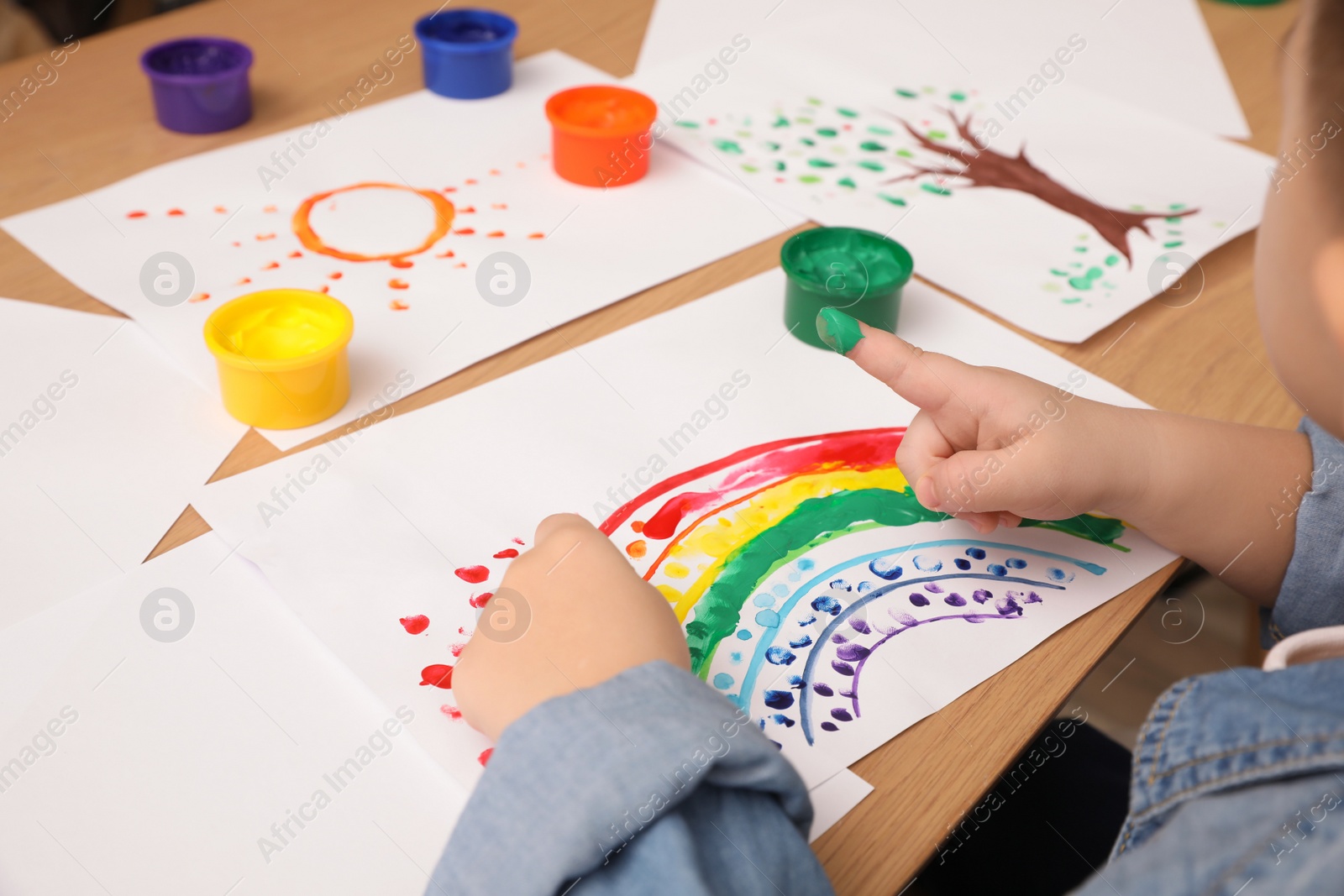 Photo of Little child painting with finger at wooden table indoors, closeup