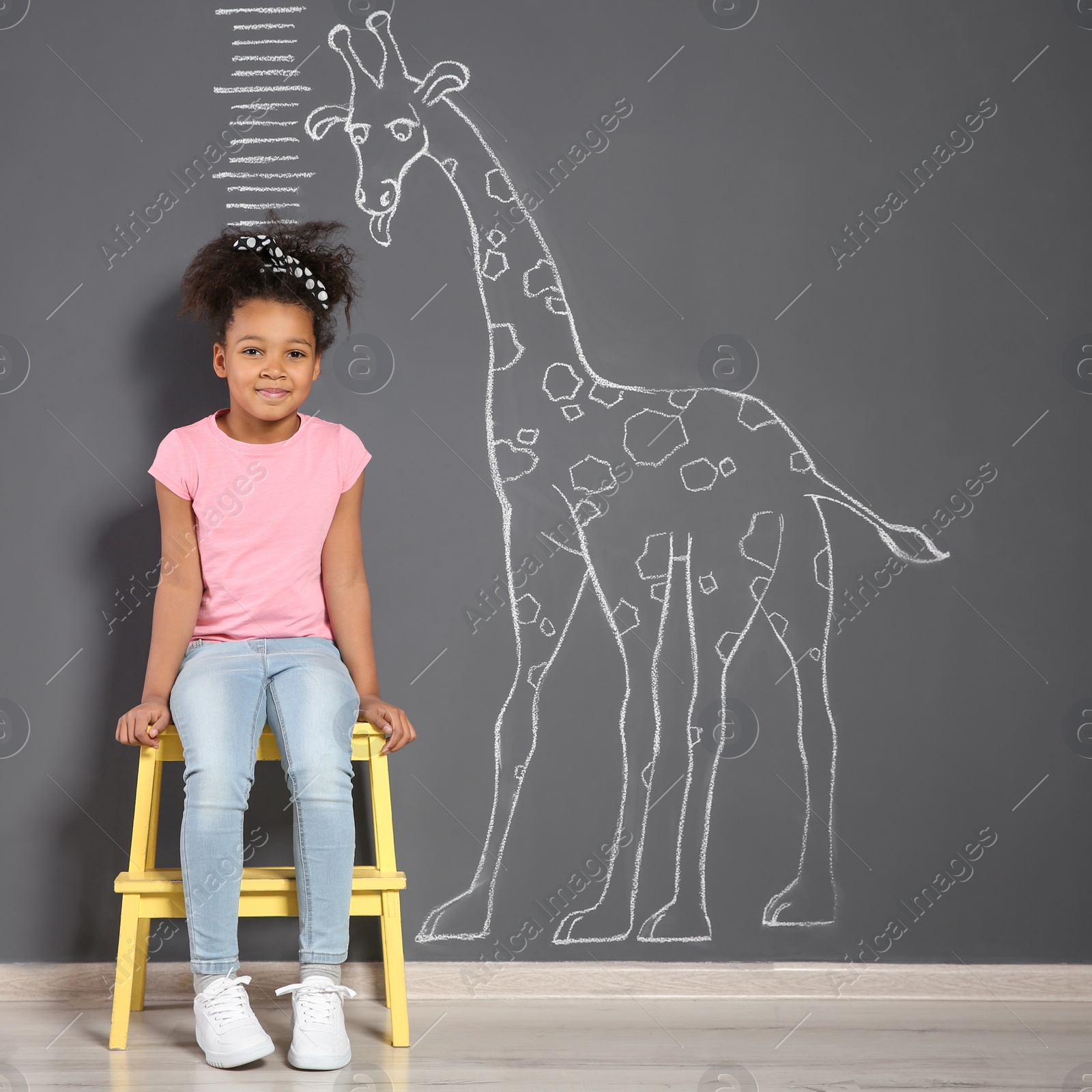 Photo of African-American child near grey wall with chalk giraffe drawing and height meter