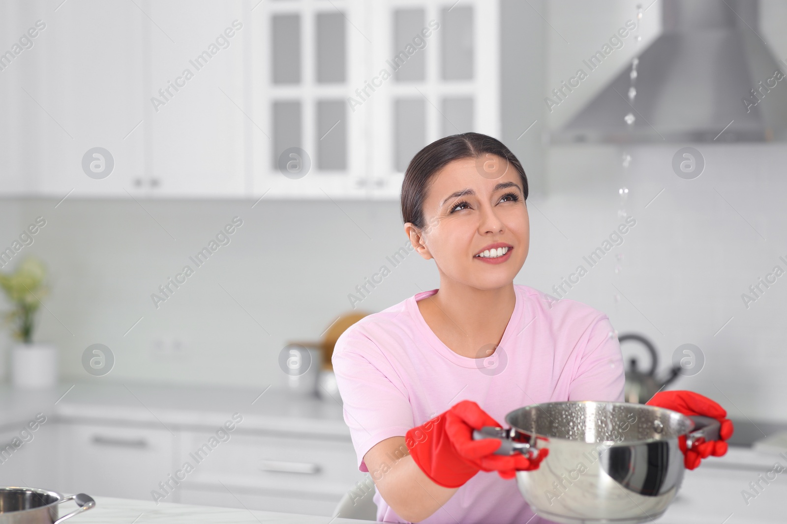 Photo of Young woman collecting leaking water from ceiling in kitchen, space for text. Time to call roof repair service