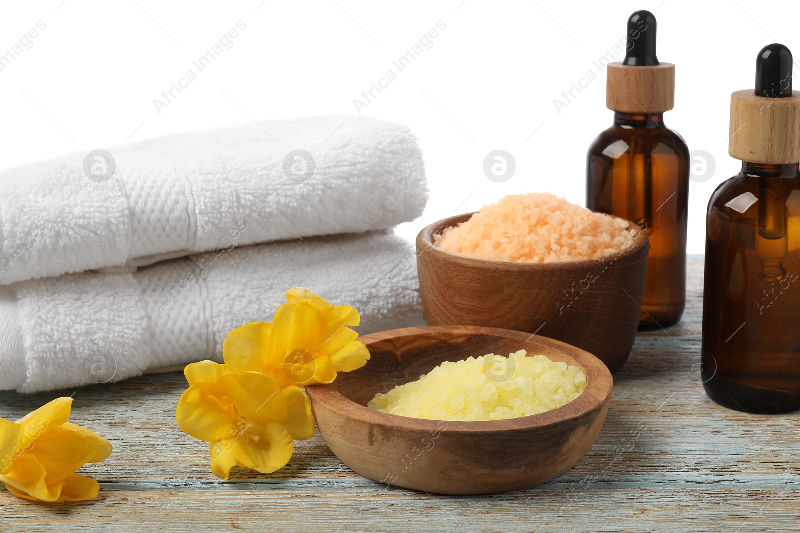 Photo of Natural sea salt in bowls and other spa supplies on wooden table against white background