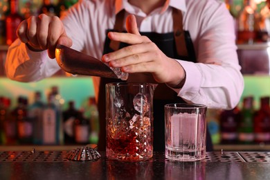 Photo of Alcoholic cocktail making. Bartender adding ice cubes into mixing glass at counter in bar, closeup