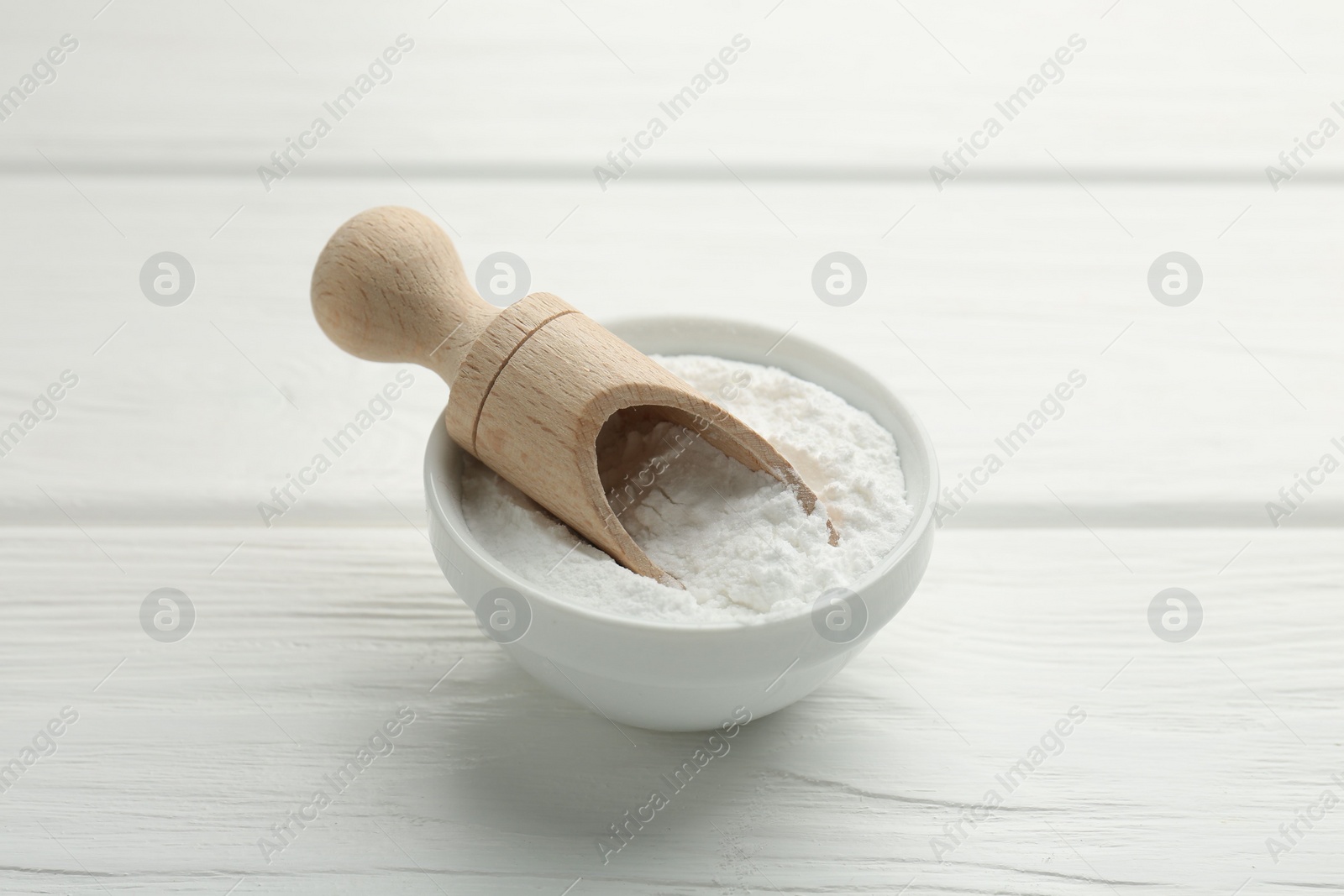 Photo of Baking powder in bowl and scoop on white wooden table