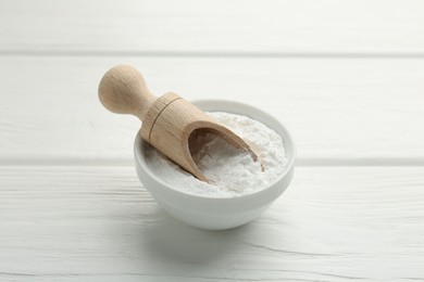 Baking powder in bowl and scoop on white wooden table