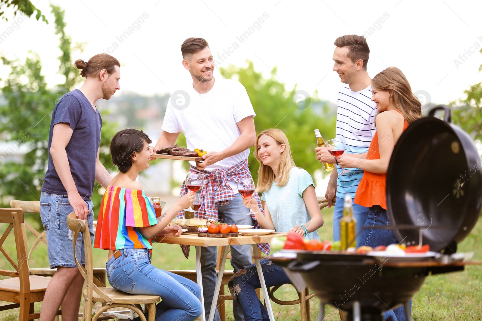 Photo of Young people having barbecue with modern grill outdoors