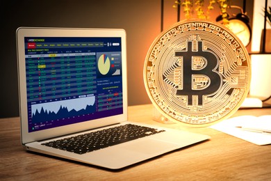 Image of Big bitcoin, laptop with trading information on screen and stationery on wooden table