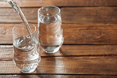 Photo of Pouring water into glass on wooden table, space for text