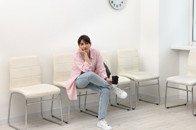 Woman with cup of drink waiting for appointment indoors