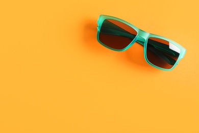 Photo of Stylish sunglasses on orange background, top view. Space for text