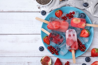 Flat lay composition with fruit and berry ice pops on white wooden table. Space for text