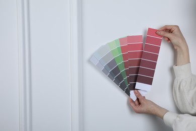 Photo of Woman with paint chips choosing color near white wall, closeup. Interior design