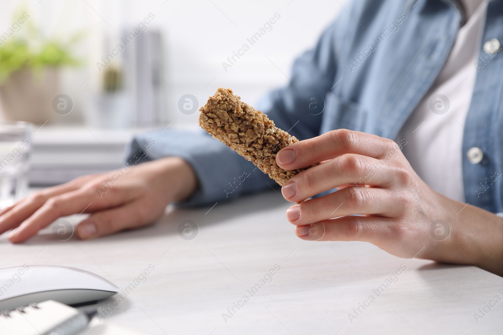Photo of Woman holding tasty granola bar at light table indoors, closeup