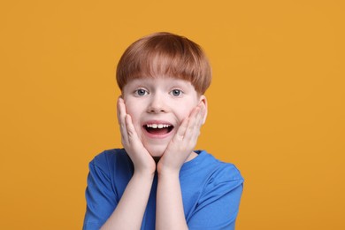 Portrait of surprised little boy on orange background