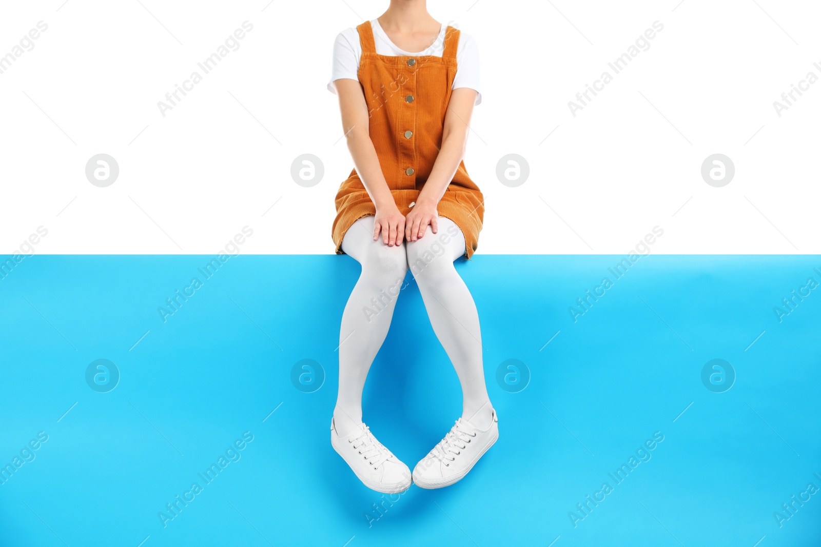 Photo of Woman wearing white tights and stylish shoes sitting on color background, closeup