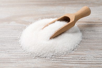 Pile of granulated sugar and scoop on light wooden table