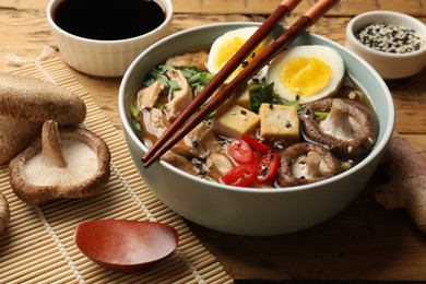 Photo of Bowl of delicious ramen and ingredients on wooden table, closeup. Noodle soup