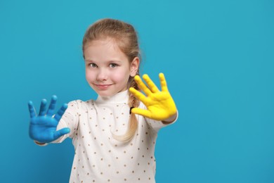 Photo of Little girl with hands painted in Ukrainian flag colors on light blue background, space for text. Love Ukraine concept