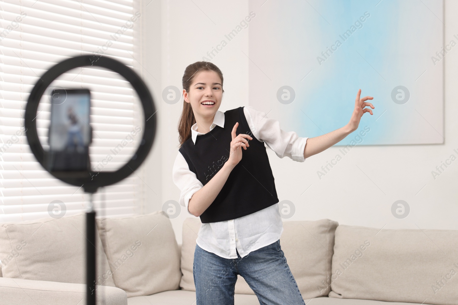 Photo of Smiling teenage blogger dancing while streaming at home