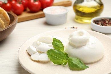 Photo of Delicious burrata cheese with basil served on white wooden table, closeup