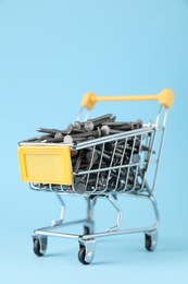 Photo of Metal nails in shopping cart on light blue background, closeup